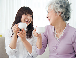 Older and younger woman holding teacups and smiling at each other.