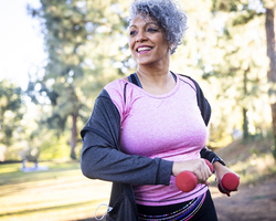 A smiling woman walks outdoors while holding hand weights.