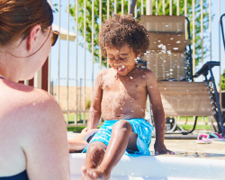 Woman watching a young boy splash his feet in a pool.