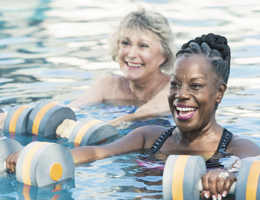 Two smiling women in a pool, holding exercise floats.