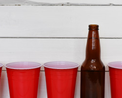 A row of empty red plastic cups and an empty beer bottle