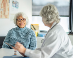 A smiling older woman talks to a doctor.