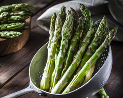 A bunch of asparagus in a steamer pan. More asparagus lies on a cutting board.