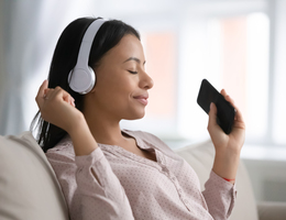 A photo of a woman sitting on a couch and listening to headphones.