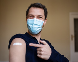 A masked man points to the bandage on his arm.