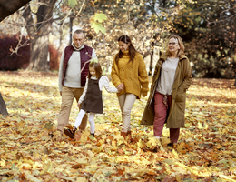 A multigenerational family walks through fall leaves.