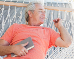 A smiling man reclines on a hammock, holding a book.