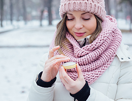 A woman outdoors in winter clothes applies lip balm