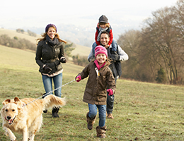 A mom, dad and two girls dressed in winter clothing running outside with their dog.