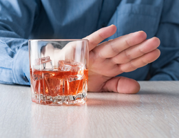 A hand pushes away a glass of scotch 