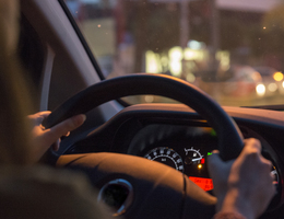 Over-the-shoulder view of a driver’s hands on the steering wheel.